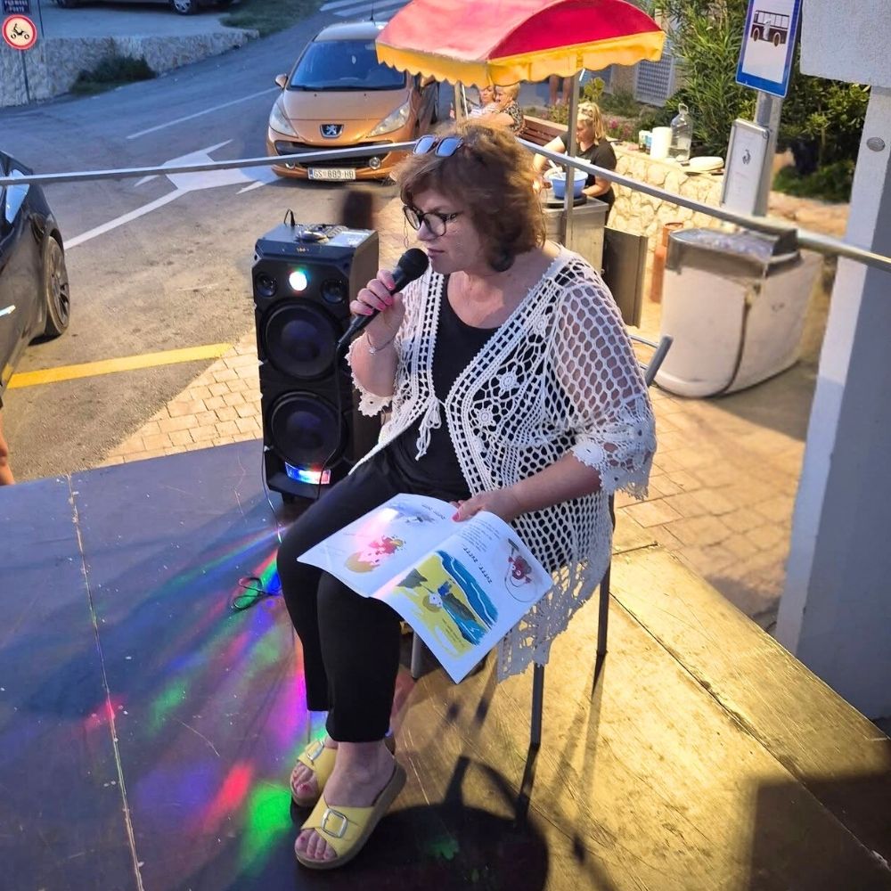 Gostovanje u Metajni – Maja Cimbal čita djeci na ljetnoj pozornici na rivi, uz priču, ples i pjesmu