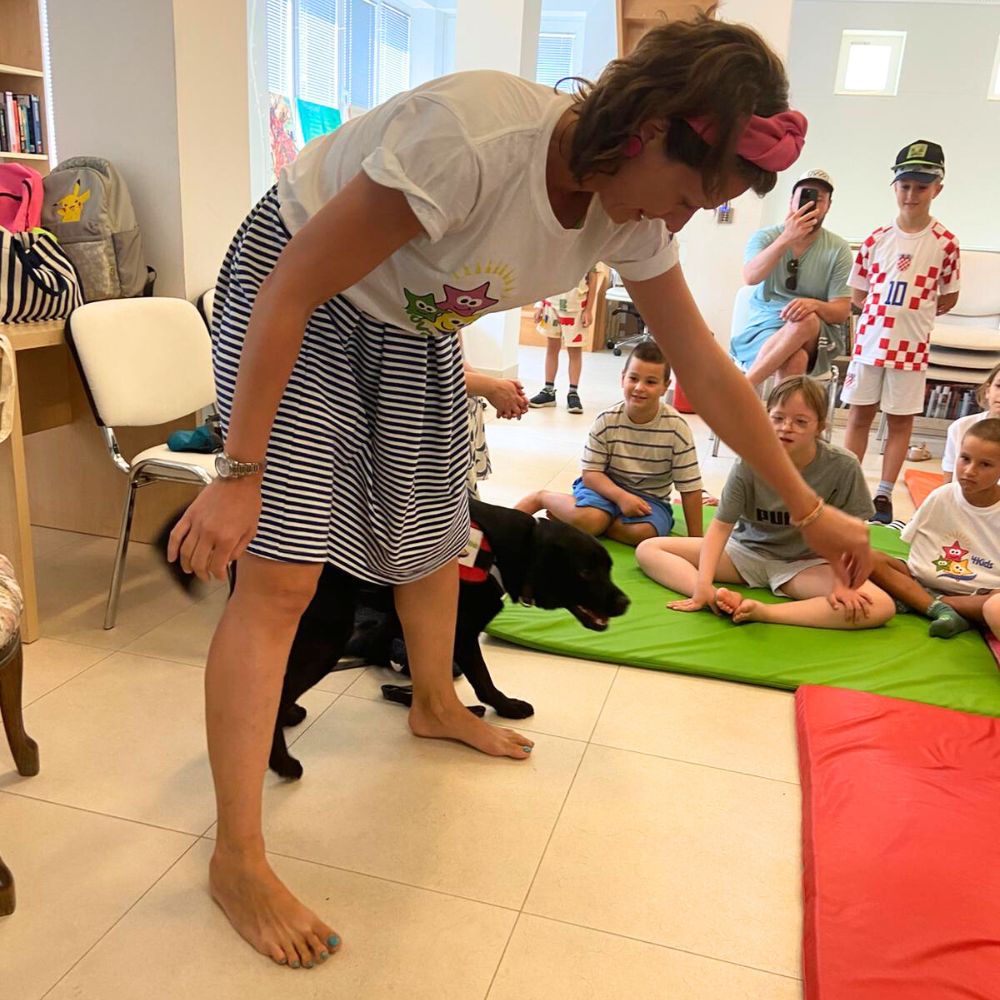 Novalja4Kids 2025 u Gradskoj knjižnici Novalja: Maja Cimbal priča djeci; Tira, terapijski pas, sudjeluje s voditeljicom Maide Arslanagić.