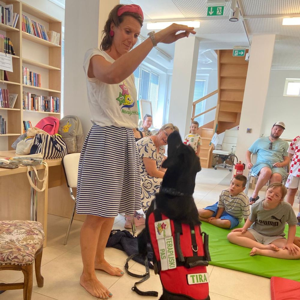 Novalja4Kids 2025 u Gradskoj knjižnici Novalja: Maja Cimbal priča djeci; Tira, terapijski pas, sudjeluje s voditeljicom Maide Arslanagić.