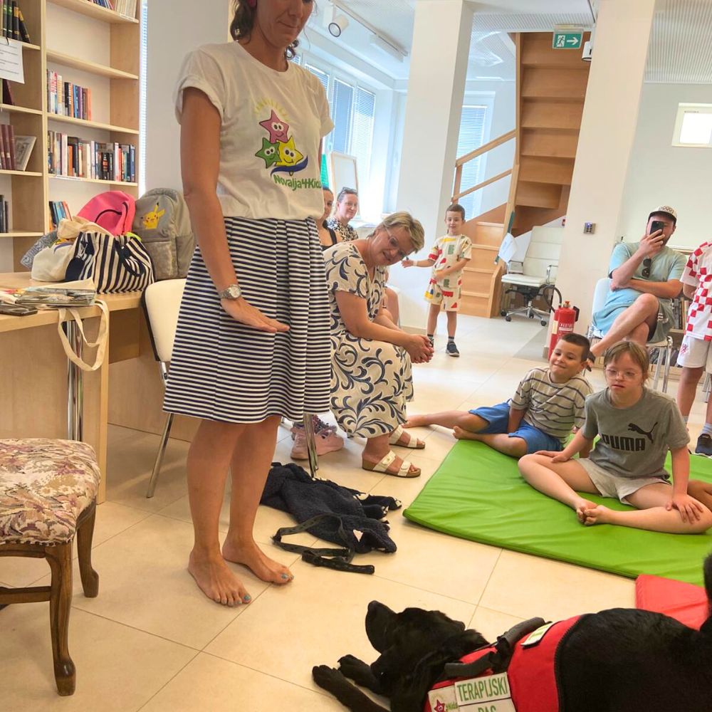Novalja4Kids 2025 u Gradskoj knjižnici Novalja: Maja Cimbal priča djeci; Tira, terapijski pas, sudjeluje s voditeljicom Maide Arslanagić.