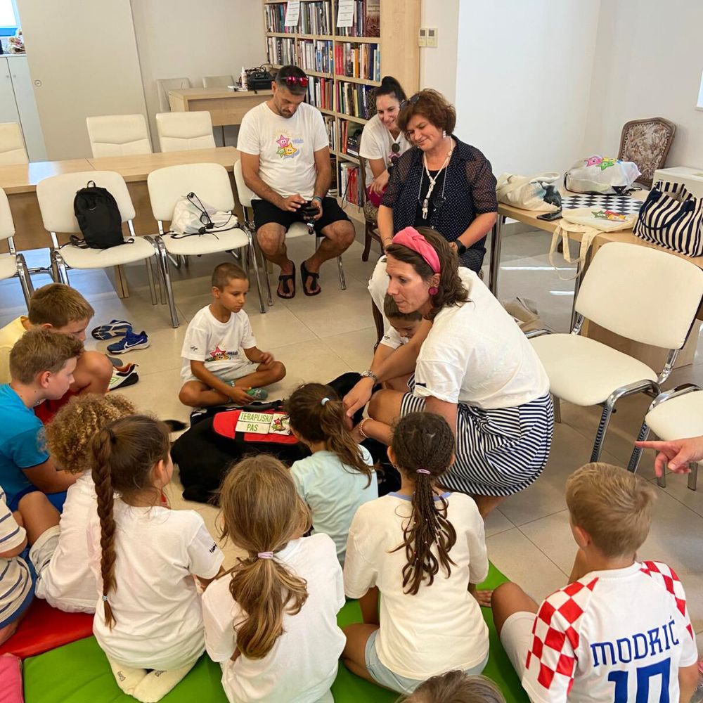 Novalja4Kids 2025 u Gradskoj knjižnici Novalja: Maja Cimbal priča djeci; Tira, terapijski pas, sudjeluje s voditeljicom Maide Arslanagić.
