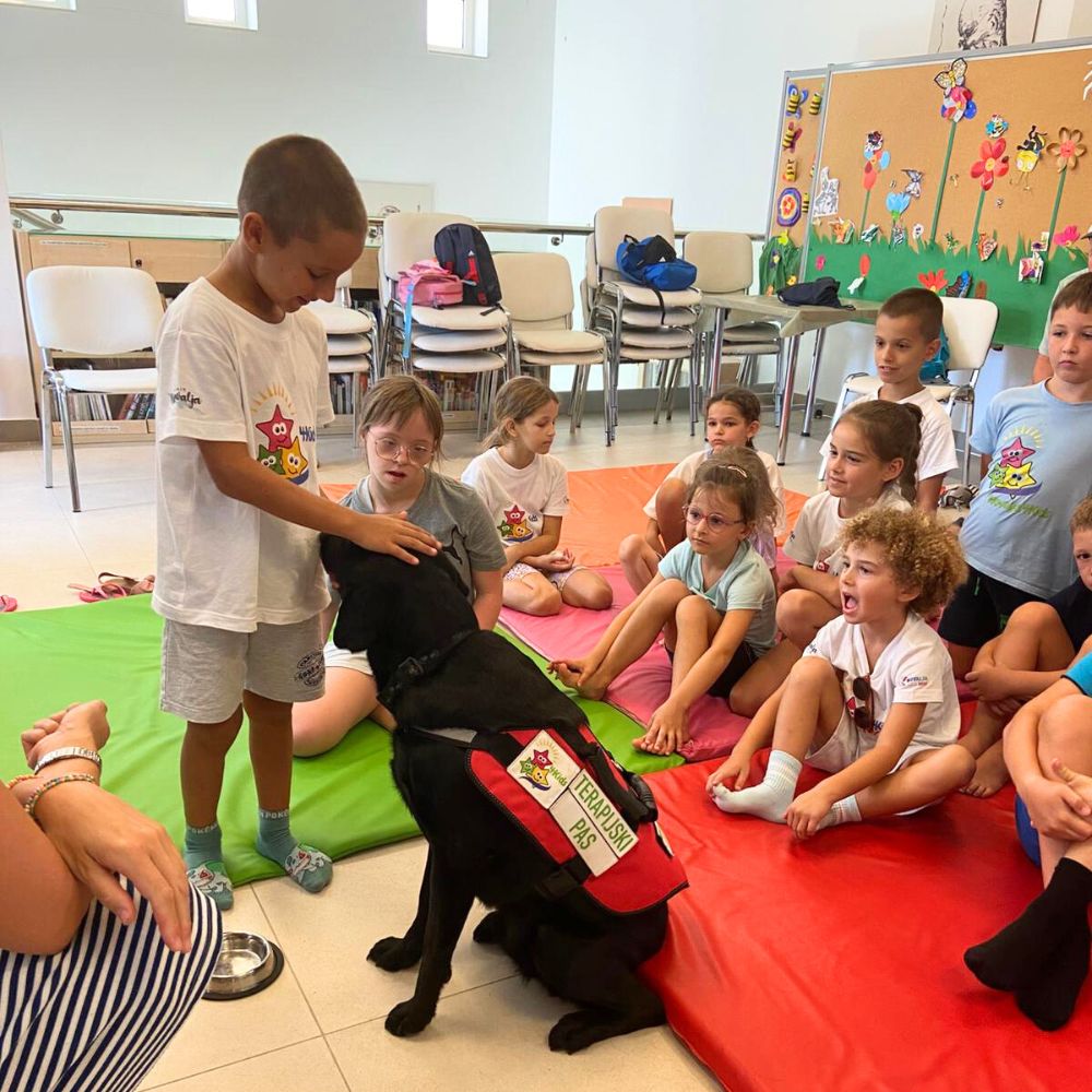 Novalja4Kids 2025 u Gradskoj knjižnici Novalja: Maja Cimbal priča djeci; Tira, terapijski pas, sudjeluje s voditeljicom Maide Arslanagić.