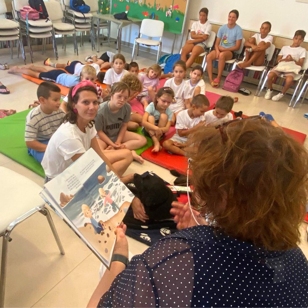 Novalja4Kids 2025 u Gradskoj knjižnici Novalja: Maja Cimbal priča djeci; Tira, terapijski pas, sudjeluje s voditeljicom Maide Arslanagić.