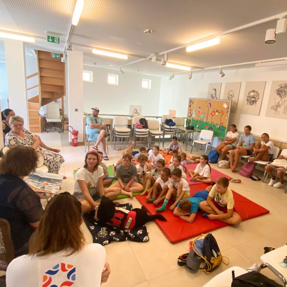 Novalja4Kids 2025 u Gradskoj knjižnici Novalja: Maja Cimbal priča djeci; Tira, terapijski pas, sudjeluje s voditeljicom Maide Arslanagić.
