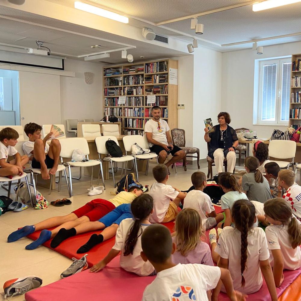 Novalja4Kids 2025 u Gradskoj knjižnici Novalja: Maja Cimbal priča djeci; Tira, terapijski pas, sudjeluje s voditeljicom Maide Arslanagić.