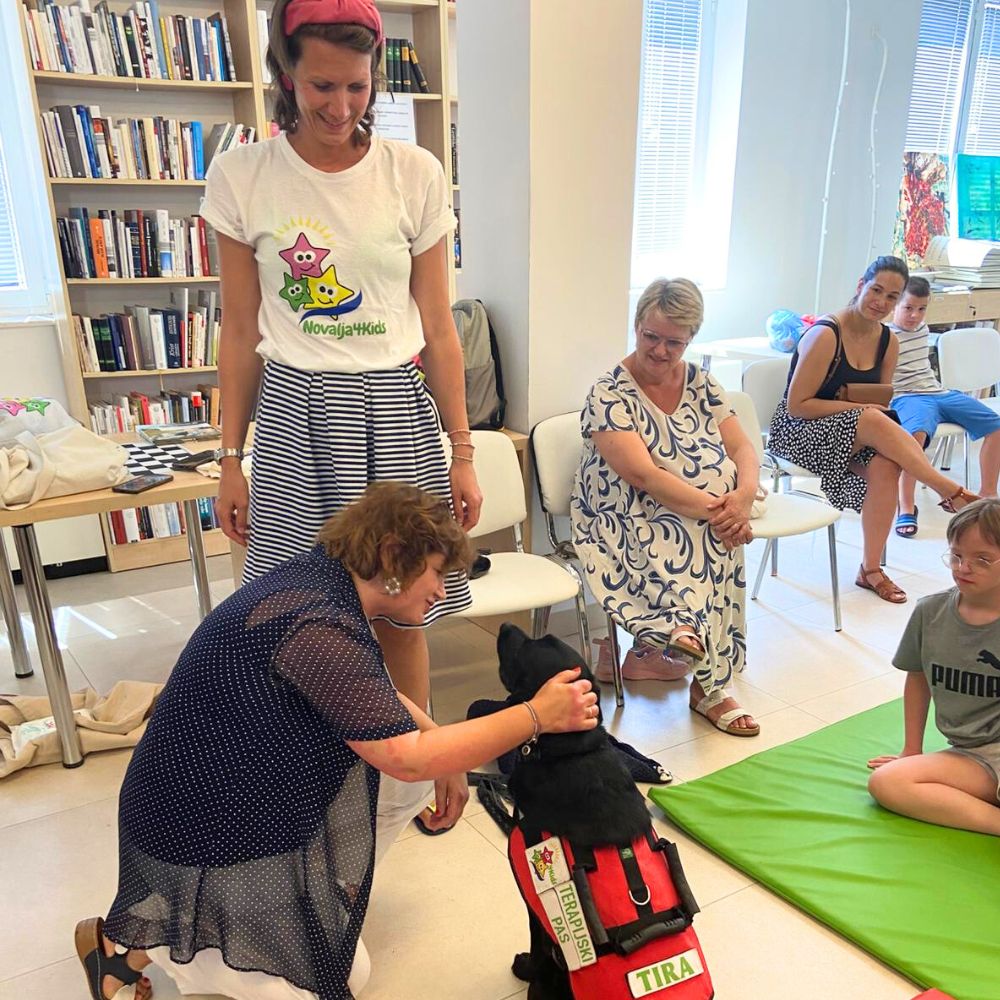 Novalja4Kids 2025 u Gradskoj knjižnici Novalja: Maja Cimbal priča djeci; Tira, terapijski pas, sudjeluje s voditeljicom Maide Arslanagić.