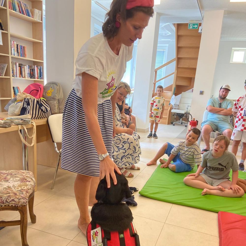 Novalja4Kids 2025 u Gradskoj knjižnici Novalja: Maja Cimbal priča djeci; Tira, terapijski pas, sudjeluje s voditeljicom Maide Arslanagić.